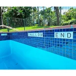 Glazed porcelain "Shallow End" warning tile installed along the pool coping for safety.